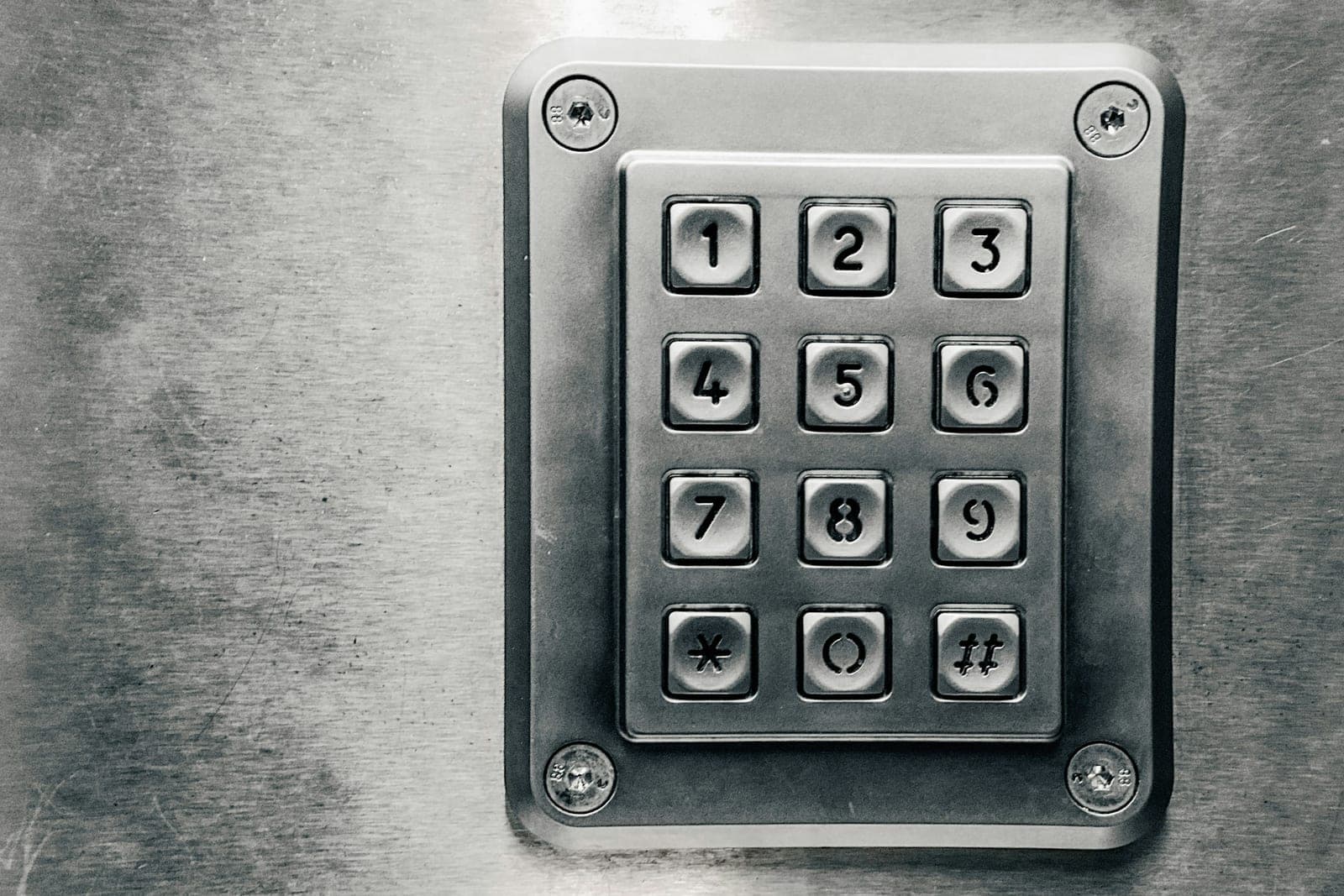 Close-up of a vandal-resistant stainless-steel PIN keypad mounted on a brushed metal door panel.