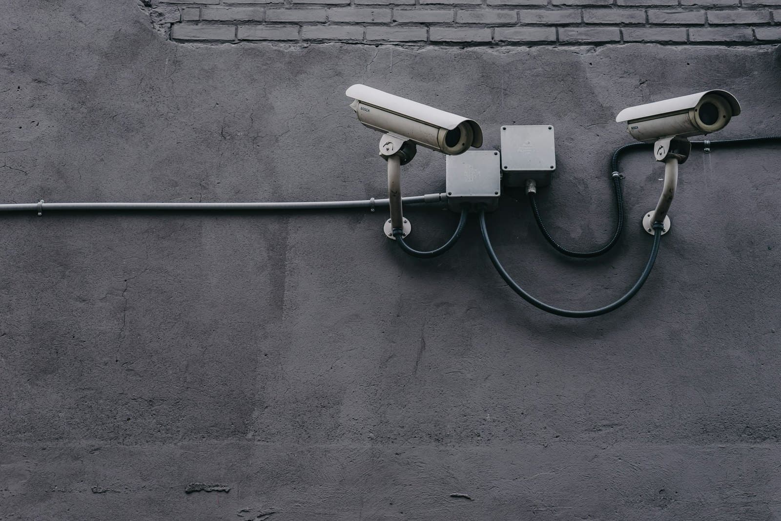 Two bullet security cameras on a grey wall, wired through conduit and junction boxes.